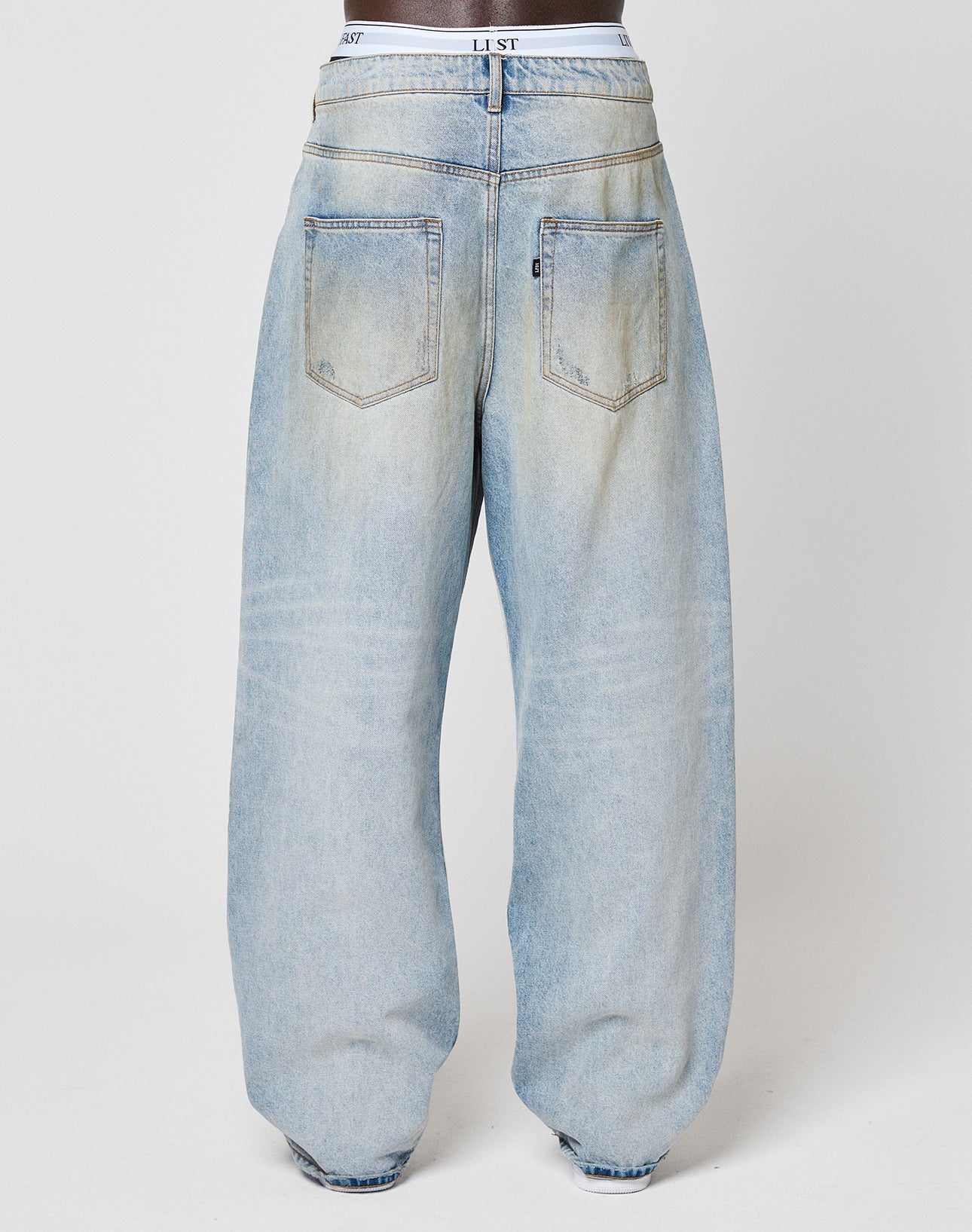 Back view of a person in LIVE FAST DIE YOUNG’s LFDY Baggy Denim, light-wash blue jeans with two back pockets and a white waistband, standing against a plain white background.
