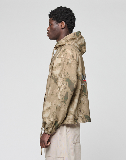 A person in profile faces left, wearing the LIVE FAST DIE YOUNG LFDY Camo Halfzip Jacket with an Oversize Fit and drawstrings, paired with pale pants, set against a plain light background.