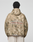 A person is seen from behind wearing the LIVE FAST DIE YOUNG LFDY Camo Halfzip Jacket, an oversize tan and green camouflage piece with a hood and “Approval GUARANTEED Credit Score Irrelevant” on the back, paired with light-colored pants.