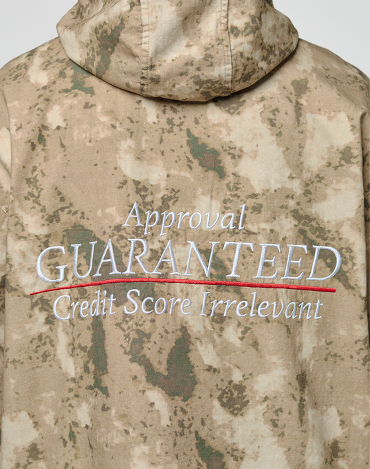 The back of the LFDY Camo Halfzip Jacket by LIVE FAST DIE YOUNG, in an oversize fit and 100% cotton, features green/tan camo with “Approval GUARANTEED Credit Score Irrelevant” embroidered—GUARANTEED underlined in red.