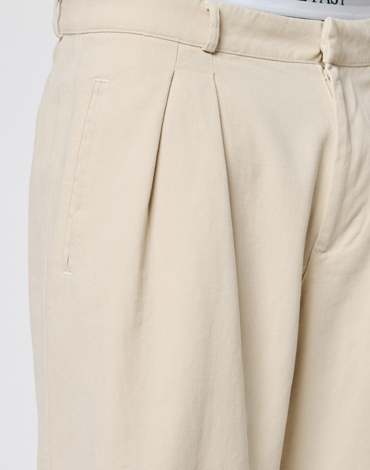 Close-up of beige Wide Chino trousers by LIVE FAST DIE YOUNG in 100% cotton, featuring a soft, slightly textured fabric, Doppel-Bundfalte waistband with belt loops, front pleats, and a side pocket.