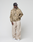 A person in a black cap, wide beige pants, white sneakers, and the LIVE FAST DIE YOUNG LFDY Camo Halfzip Jacket stands against a plain light gray background, looking to the side with one hand in their pocket.
