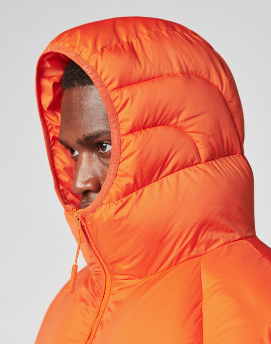 Someone wearing the LIVE FAST DIE YOUNG Live Fast Puffer Jacket in bright orange, with an oversized fit and hood up, partially zipped, looks to the side against a plain light background.