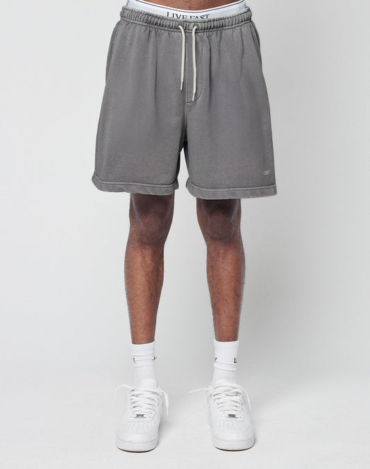 A person wears LIVE FAST DIE YOUNG Basic Sweat Shorts in gray with an elastic waistband, paired with white socks and sneakers. Only the lower half of their body is shown against a plain light background.