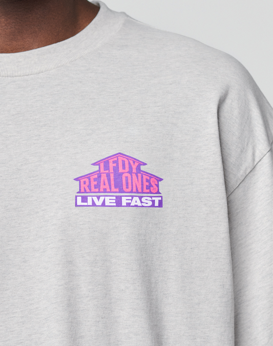 A close-up of the LFDY Real Ones Tee by LIVE FAST DIE YOUNG—an oversized, light grey 100% cotton shirt with a pink and purple "LFDY REAL ONES LIVE FAST" chest graphic and a subtle flag label detail.
