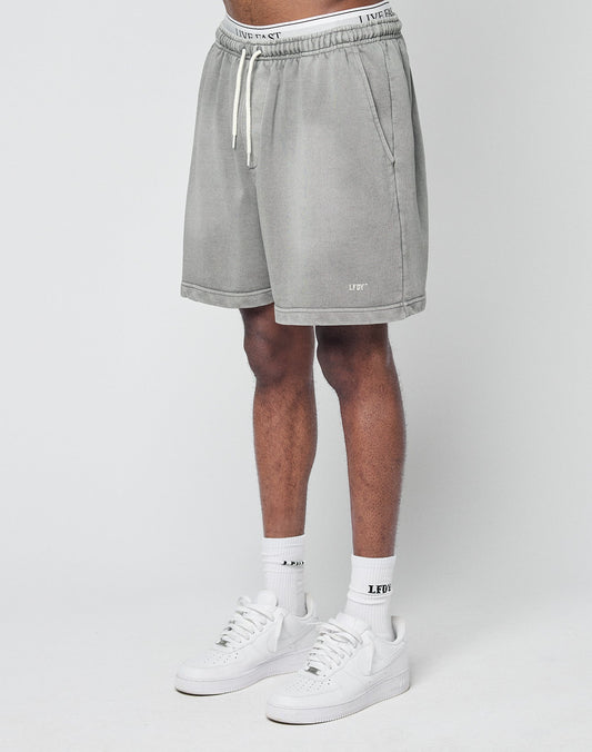 A person wearing LIVE FAST DIE YOUNGs Basic Sweat Shorts in light gray, LFDY logo white socks, and white sneakers stands against a plain white background, with only their lower half visible. | model