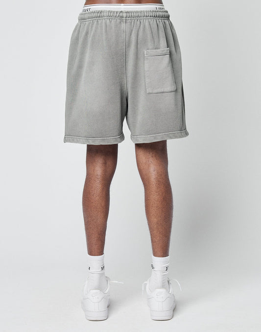 A person models LIVE FAST DIE YOUNG Basic Sweat Shorts in light gray, a regular fit with a back pocket, paired with white socks and sneakers, standing against a plain light gray background, shown from the back waist down.