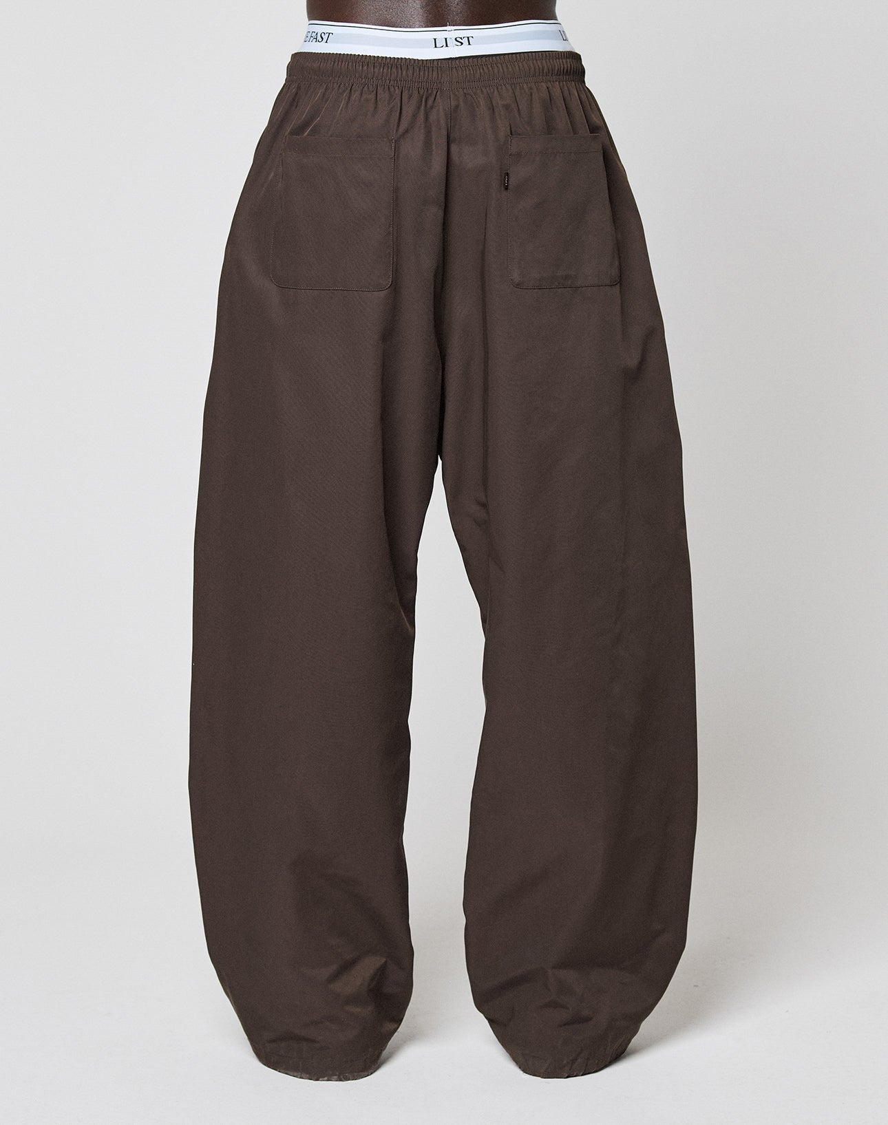 The LIVE FAST DIE YOUNG Baggy Nylon Pants feature a loose, wide fit, Elastikbund waistband, and two large back pockets. Shown on a mannequin with a plain light background—ideal for fans of comfort and relaxed style.