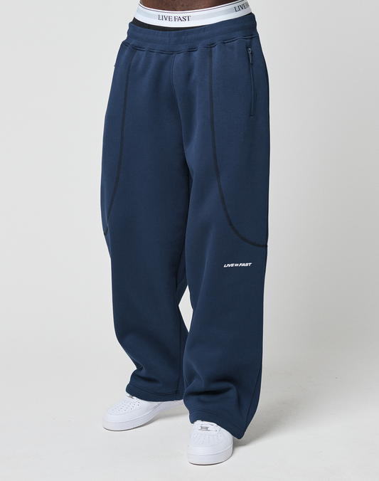 Wearing LFDY Active Fleece Jogger by LIVE FAST DIE YOUNG in wide fit navy blue with black seam details and a white LIVE FAST logo near the left knee, paired with white sneakers and visible LIVE FAST DIE YOUNG underwear waistband.