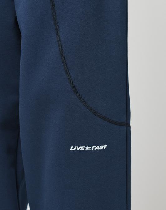Close-up of LFDY Active Fleece Jogger by LIVE FAST DIE YOUNG in navy blue, featuring black seam details, a white LIVE FAST logo with arrow motif on the thigh, and a comfortable wide fit.