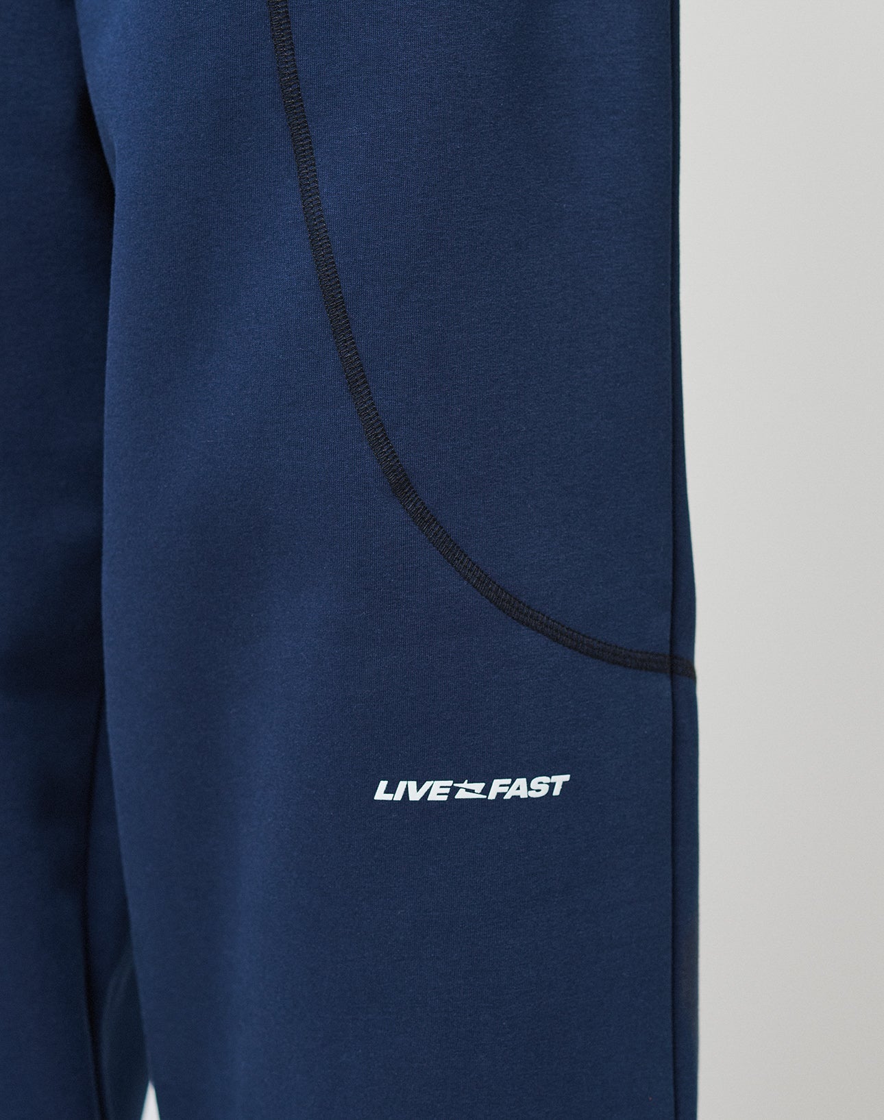 Close-up of LFDY Active Fleece Jogger by LIVE FAST DIE YOUNG, blue athletic Wide Fit hose with black seam detailing, zip pockets, and a bold white LIVE FAST logo near the pocket.