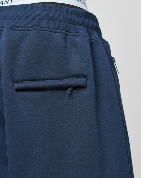 Close-up of a person in LIVE FAST DIE YOUNG's LFDY Active Fleece Jogger, a navy blue wide fit sweatpant with elastic waistband and closed back pocket, revealing a hint of white underneath. Made from soft Baumwolle for comfort.