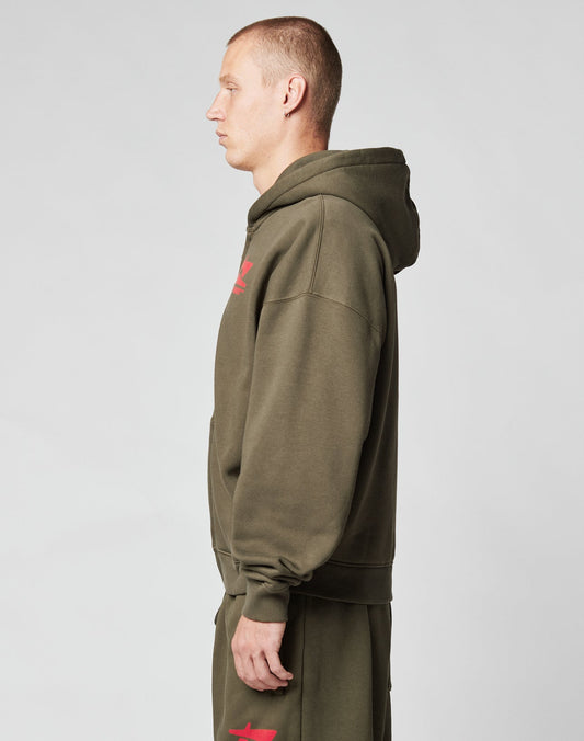A man with short hair stands in profile, wearing the LIVE FAST DIE YOUNG Live Fast Sweatsuit Jacket in olive green Oversize Fit and matching sweatpants with red front print, set against a plain light gray background.