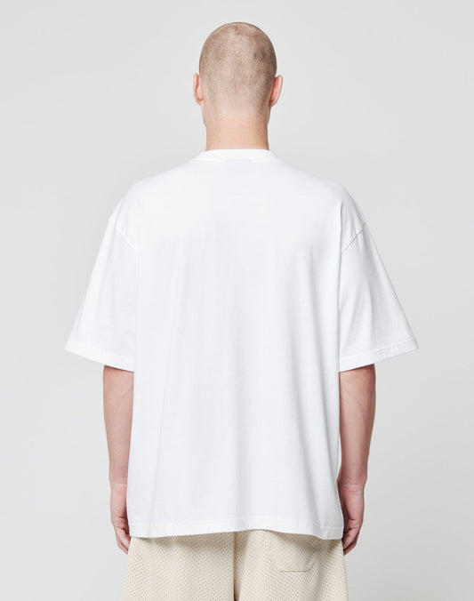 A person with a shaved head stands with their back to the camera, wearing a LIVE FAST DIE YOUNG Basic Script Tee in plain white and light-colored shorts against a plain light gray background.