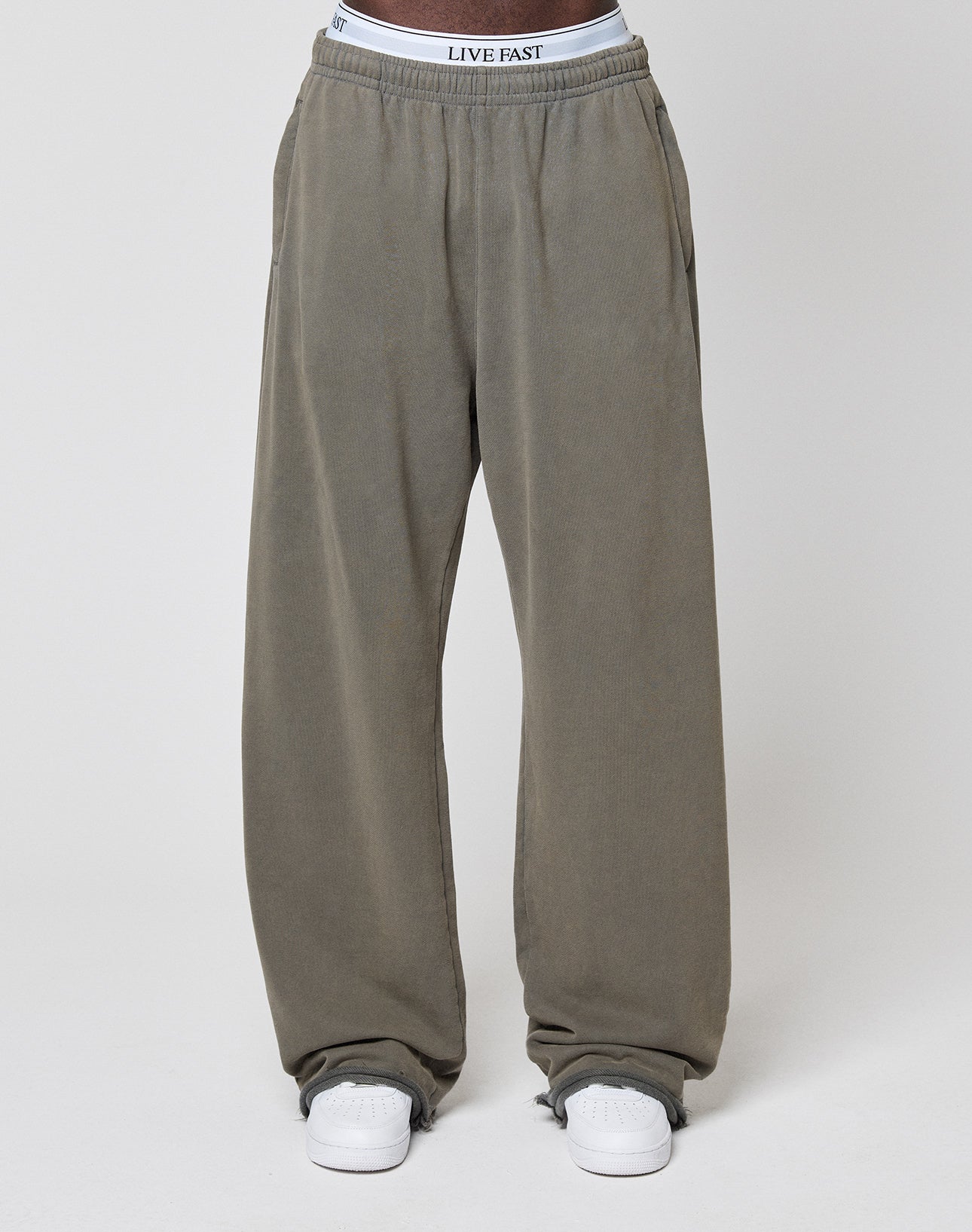 A person wears loose-fitting, grey LFDY Ripped Sweatpants by LIVE FAST DIE YOUNG, featuring an elastic waistband and 100% cotton material, paired with white sneakers against a plain light background.