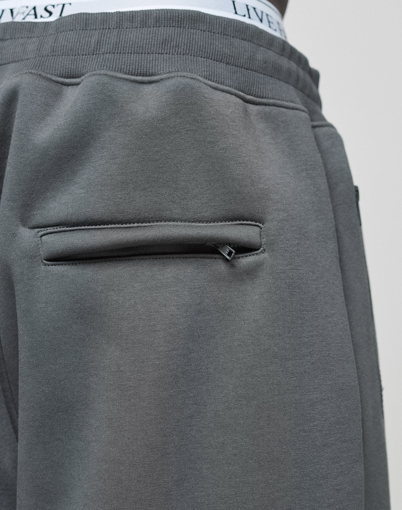Close-up of the back pocket on LFDY Active Fleece Jogger by LIVE FAST DIE YOUNG, highlighting the zippered pocket and flatlock-topstitching. The waistband of white LIVE FAST DIE YOUNG underwear is partially visible above the pants.