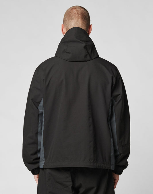A person wearing the LIVE FAST DIE YOUNG Basic Shell Jacket, featuring an oversize fit, black color, dark gray side panels, and a water-repellent zipper, is shown from the back against a plain light background.