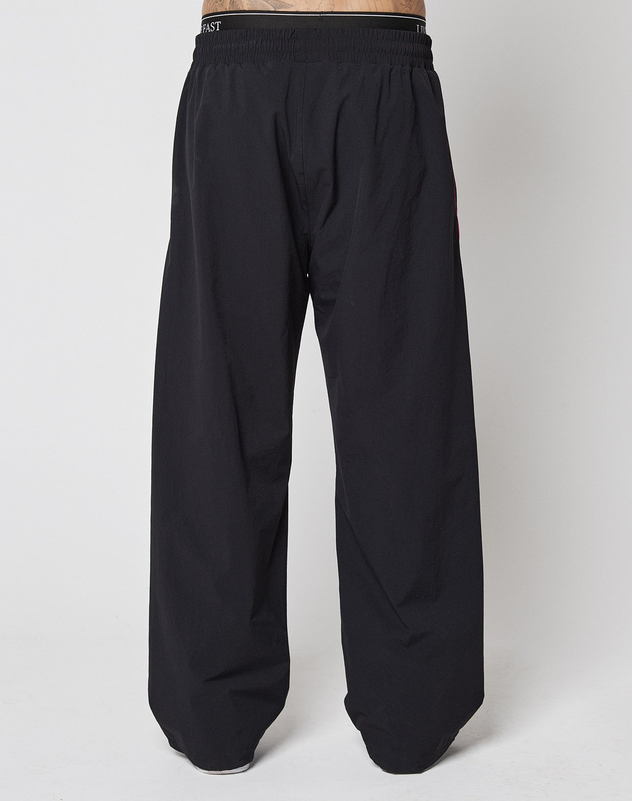 The LFDY Wavy Trackpants by LIVE FAST DIE YOUNG are wide-leg black pants with an elastic waistband, shown from the front on a plain white background. They feature a loose fit and full length that partially covers the feet.