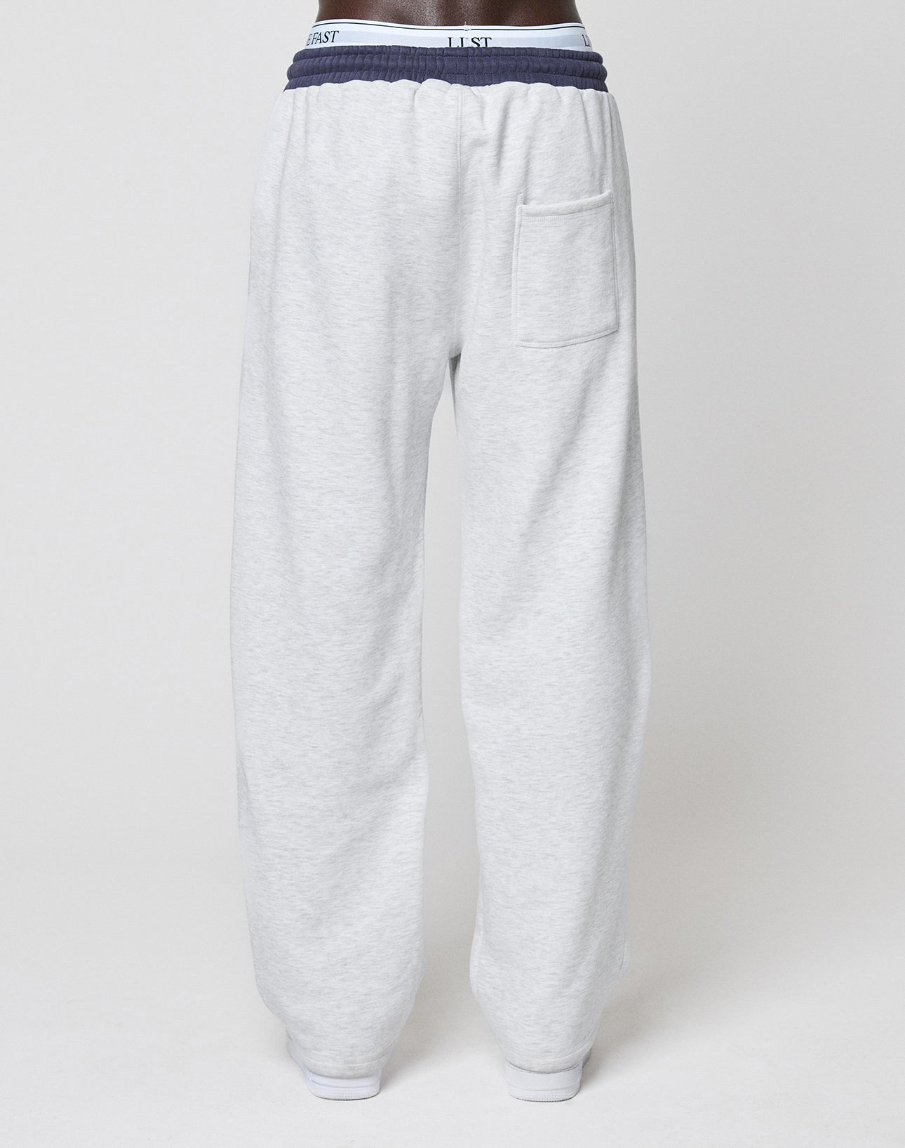 A person wearing the LFDY District Jogger by LIVE FAST DIE YOUNG in light gray with a wide fit, contrast waistband, and back pocket, photographed from behind against a plain white background.
