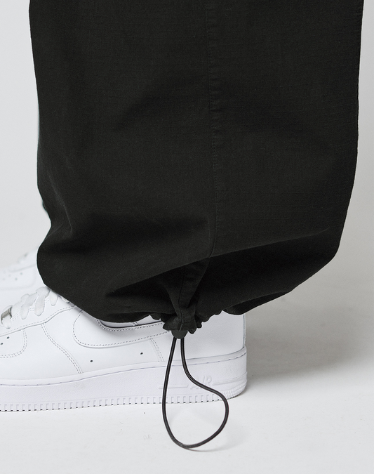 A close-up of someone in LIVE FAST DIE YOUNG’s LFDY Baggy Cargo pants with a drawstring hem and cargo pockets, styled with white sneakers against a light background.