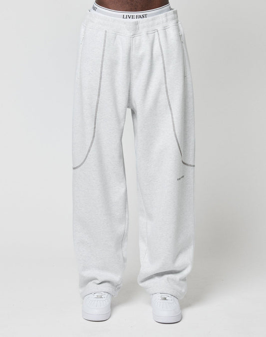 A person wears the LFDY Active Fleece Jogger by LIVE FAST DIE YOUNG—light gray, wide fit with seam details and a logo print waistband reading LIVE FAST—paired with white sneakers, against a plain white background.