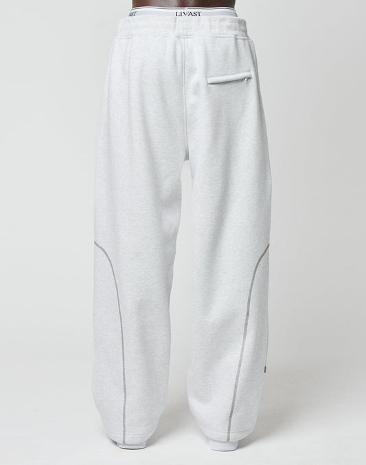Someone is seen from behind in LFDY Active Fleece Joggers by LIVE FAST DIE YOUNG. These light gray pants have a wide fit, right-side back pocket, curved seams, and a waistband with LINVAST logo print.
