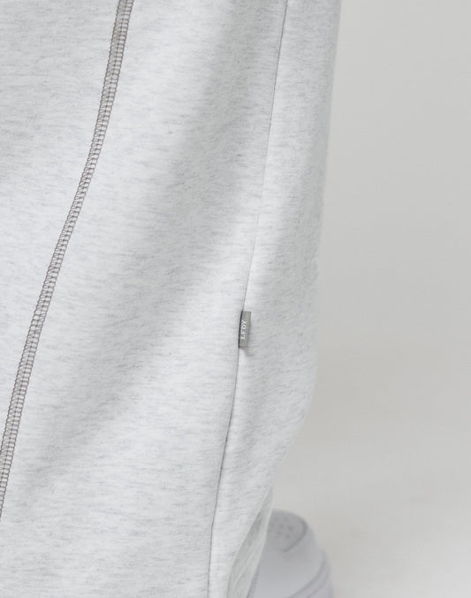 Close-up of LFDY Active Fleece Jogger by LIVE FAST DIE YOUNG in light gray, featuring a wide fit, visible side seam with contrast stitching, and a small branded fabric tag. The lower part of a white sneaker appears at the bottom.