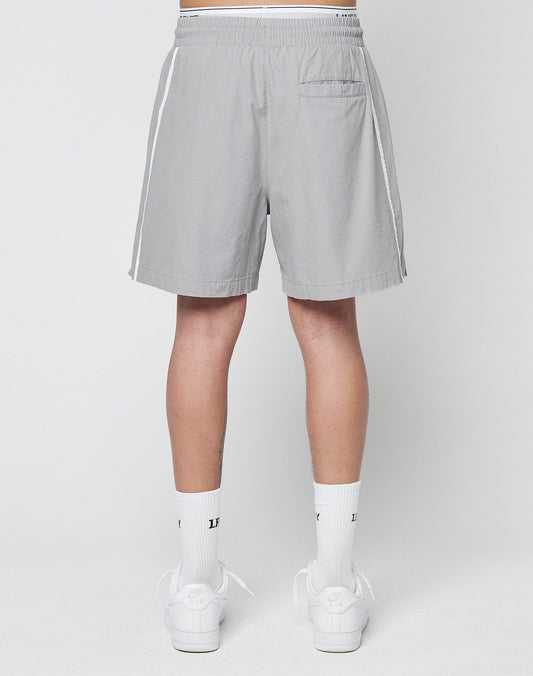 A person stands facing away in LIVE FAST DIE YOUNG Basic Cotton Shorts—light gray regular fit with white side stripes and elastic waistband—paired with white crew socks and sneakers, set against a plain light background.