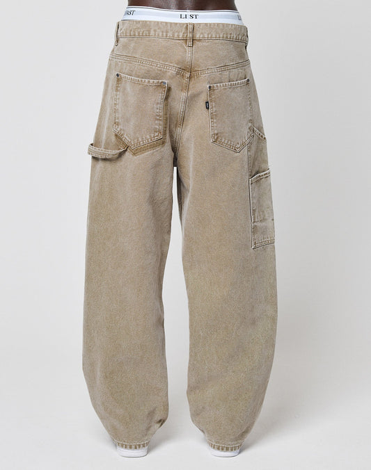 A person rocks the Carpenter Look in LIVE FAST DIE YOUNG Faded Carpenter Pants—baggy, light brown denim with large utility pockets. White LIST underwear peeks above the waist, adding a relaxed vintage vibe.