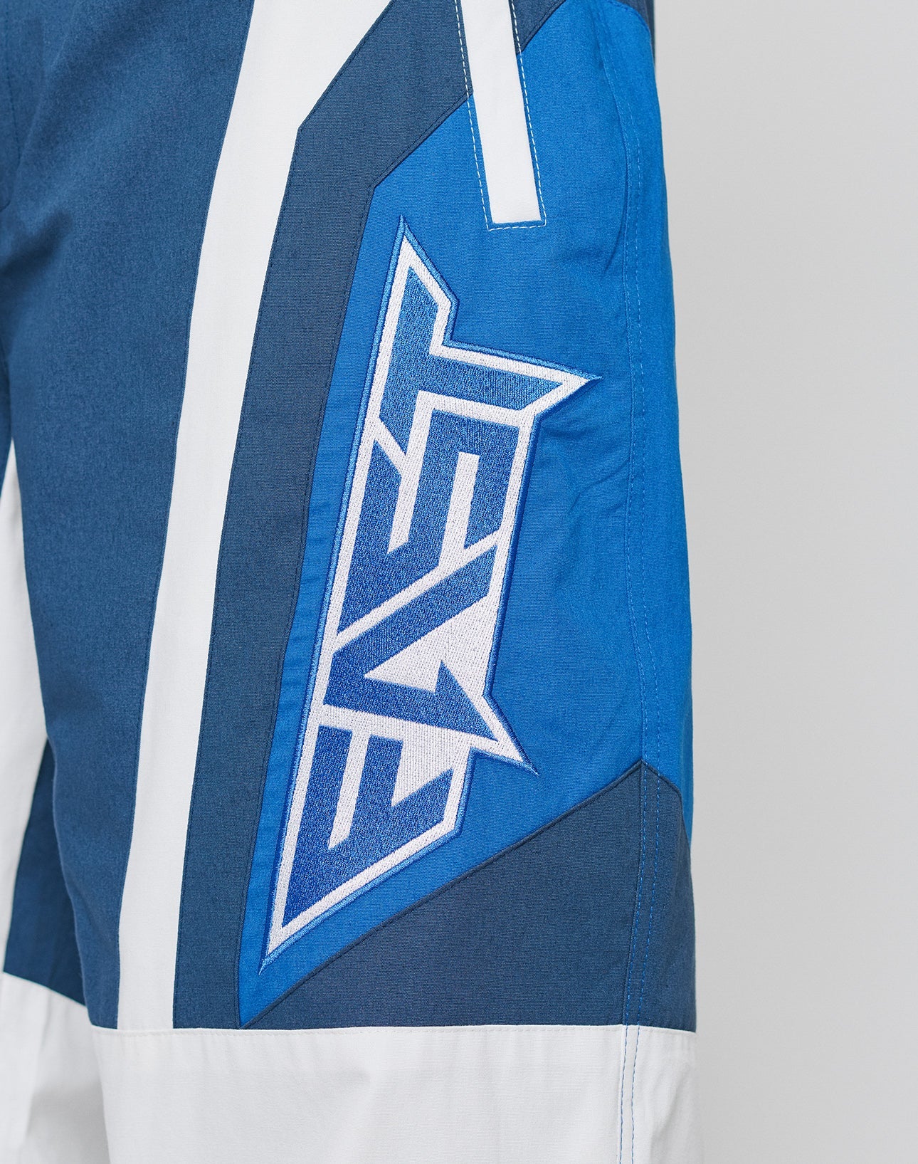 Close-up of LFDY Cross Pants by LIVE FAST DIE YOUNG—blue and white with a bold FAST patch, made from Baumwolle. Features an elastikbund, angular shapes, contrasting colors, and an oversize fit for comfort and style.