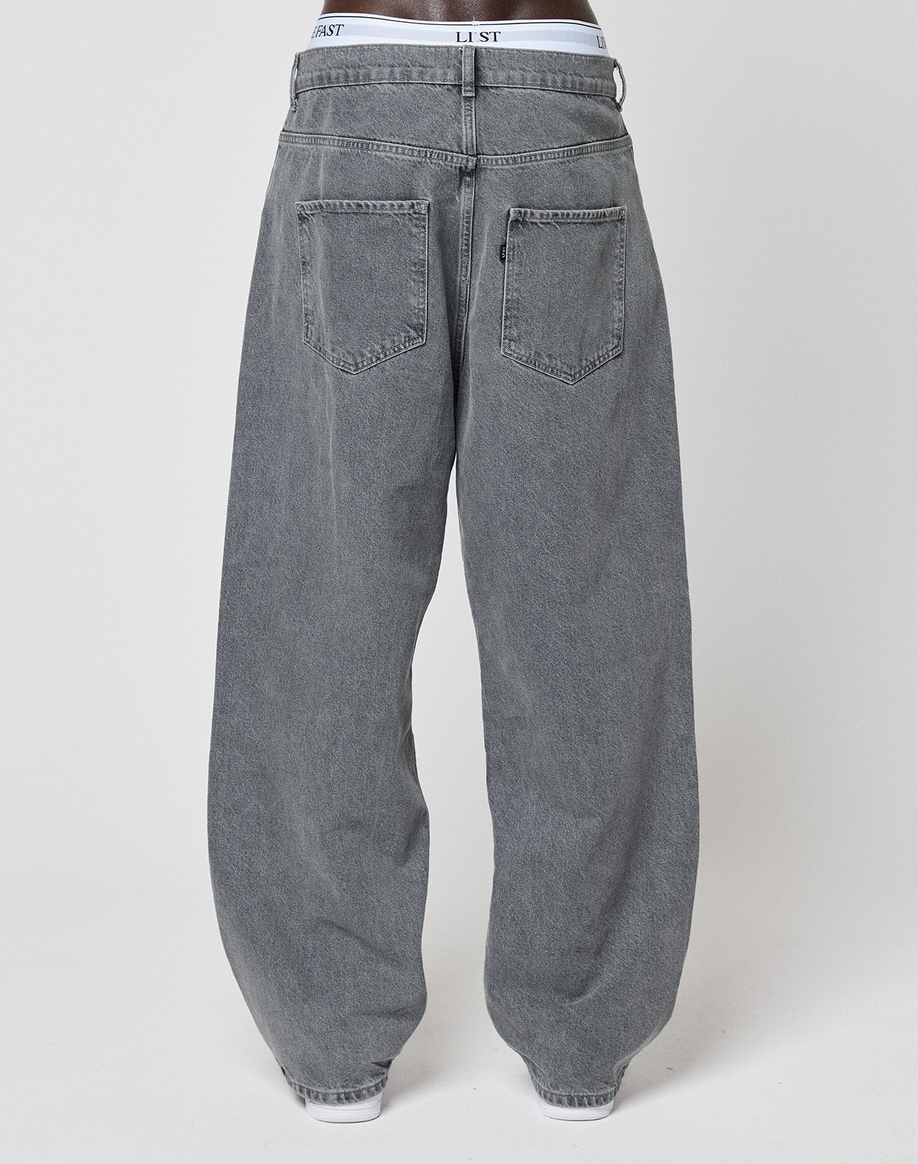 Back view of a person wearing LIVE FAST DIE YOUNG's LFDY Baggy Denim—gray, straight-leg (gerades Bein), 100% Baumwolle jeans with two rear pockets and visible white waistband. Plain, light-colored background.