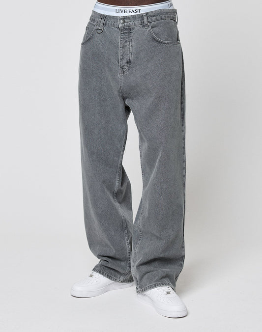 A person in LFDY Baggy Denim by LIVE FAST DIE YOUNG, paired with white sneakers and a visible white waistband reading LIVE FAST, stands against a plain light background.