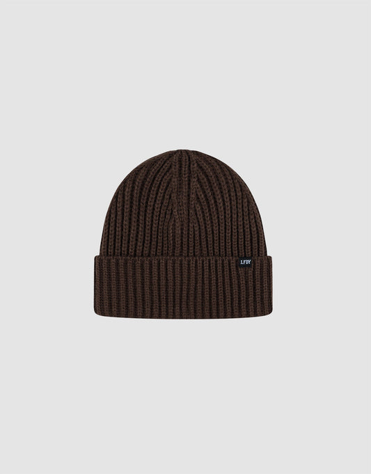 A dark brown Rib Knit Beanie by LIVE FAST DIE YOUNG in polyacryl with a folded cuff, shown on a light gray background. Features a small black tag with white text on the cuff. One Size for versatile wear.