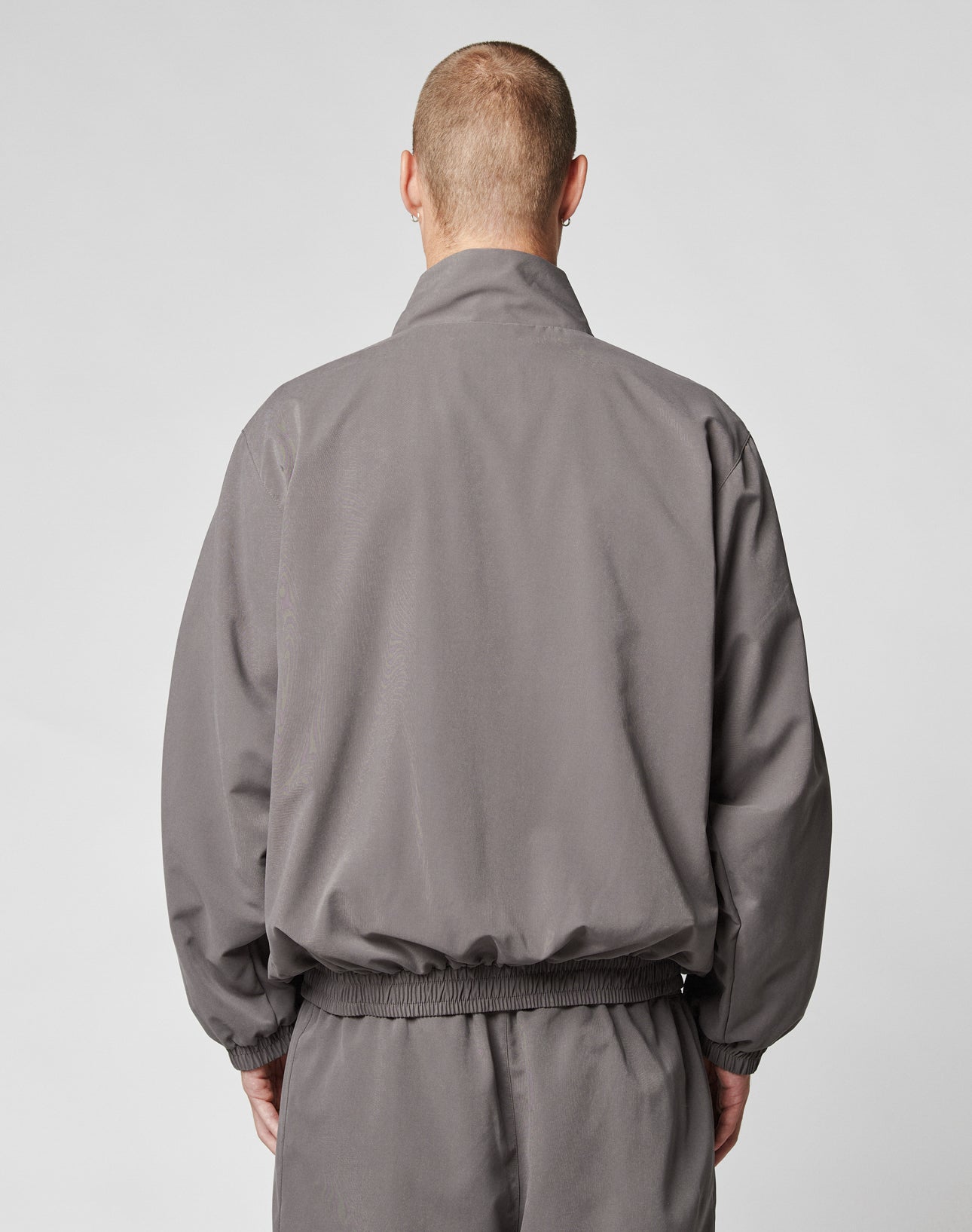 A person with short hair, seen from the back, wears an oversized gray LFDY Trackjacket and matching pants by LIVE FAST DIE YOUNG, standing against a plain light gray background.
