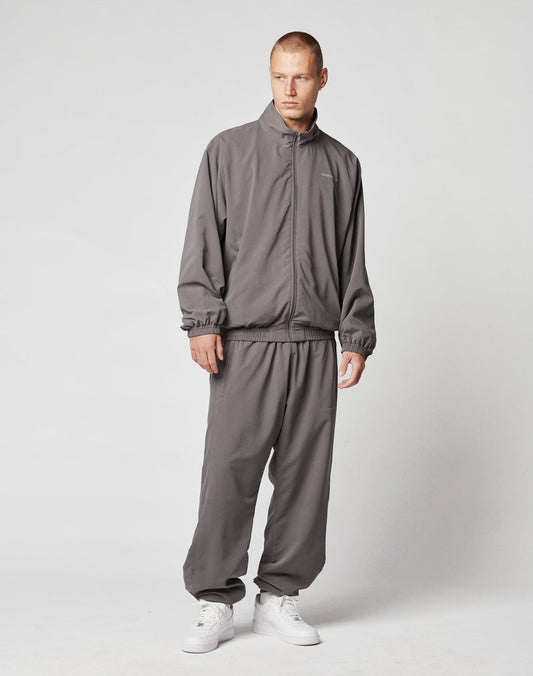 A man wearing an oversized gray LFDY Trackjacket and matching pants by LIVE FAST DIE YOUNG, paired with white sneakers, stands against a light gray background.