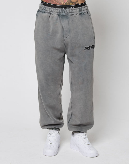 Model wears LFDY Europe Run Jogger by LIVE FAST DIE YOUNG—a grey, loose-fit sweatpant with LIVE FAST print on the left thigh and elastic cuffs, paired with white sneakers. Photo shows only lower body against a plain white background.