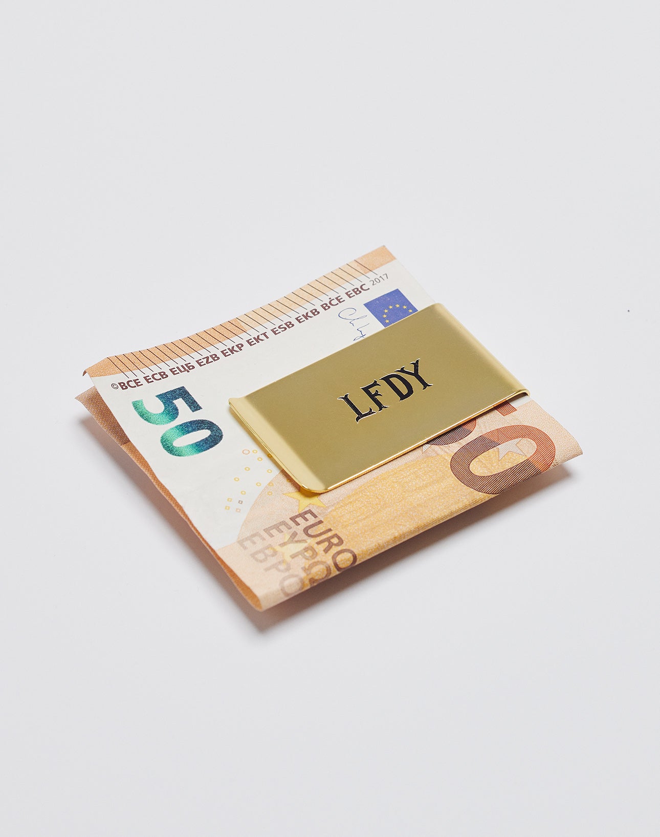 A gold Basic Money Clip by LIVE FAST DIE YOUNG (mod. LF2305-13647), aus Edelstahl mit graviertem Logo, hält gefaltete 10- und 20-Euro-Scheine auf weißem Hintergrund.