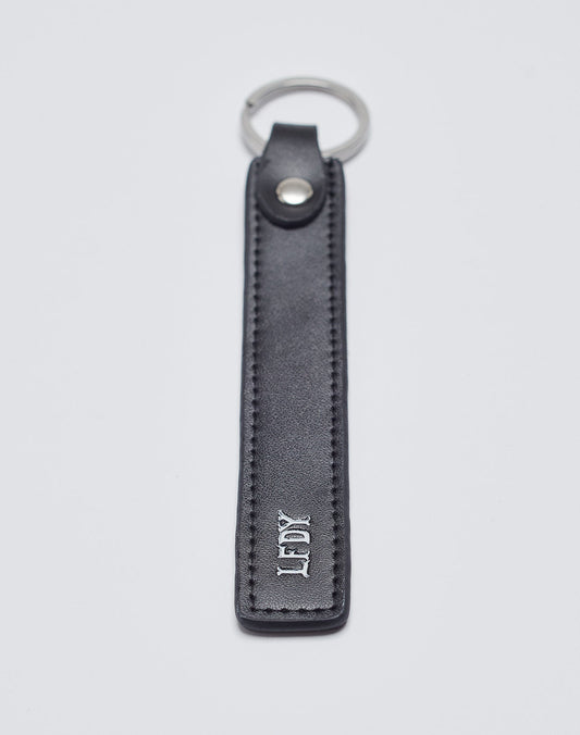 The Basic Keychain by LIVE FAST DIE YOUNG features black PU leather with visible stitching, a stainless steel ring, metal snap button, and white embossed “LDK” near the bottom for a stylish touch.