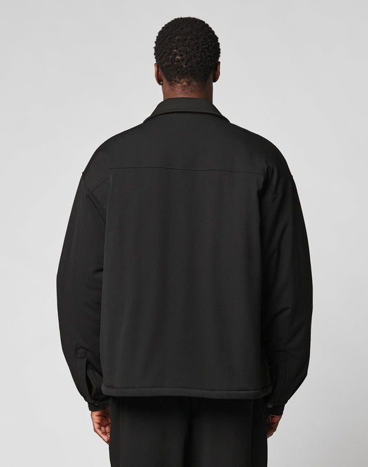 A person with short curly hair is seen from the back, wearing the LIVE FAST DIE YOUNG Padded Casual Shirt in an oversized fit and black pants, set against a plain light background.