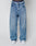 A person in LFDY Baggy Denim by LIVE FAST DIE YOUNG, blue jeans with a wide straight leg made from 100% cotton, pairs the look with white sneakers. The LIVE FAST waistband of dark underwear is visible above the jeans against a plain white background.