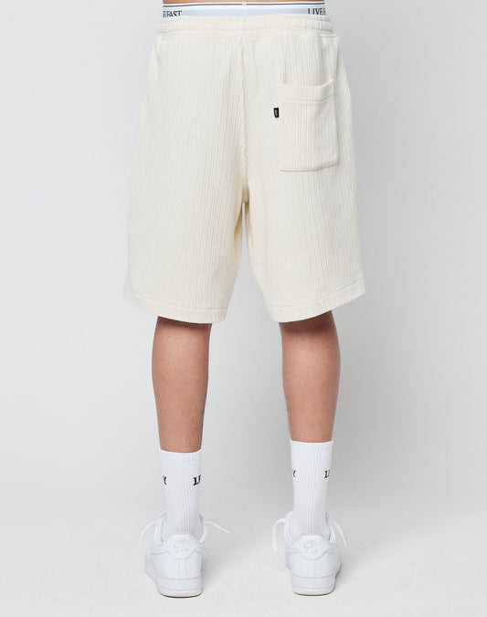 A person is shown from the back wearing off-white LIVE FAST DIE YOUNG Basic Knit Shorts with a back pocket, white crew socks, and white sneakers against a plain light background.