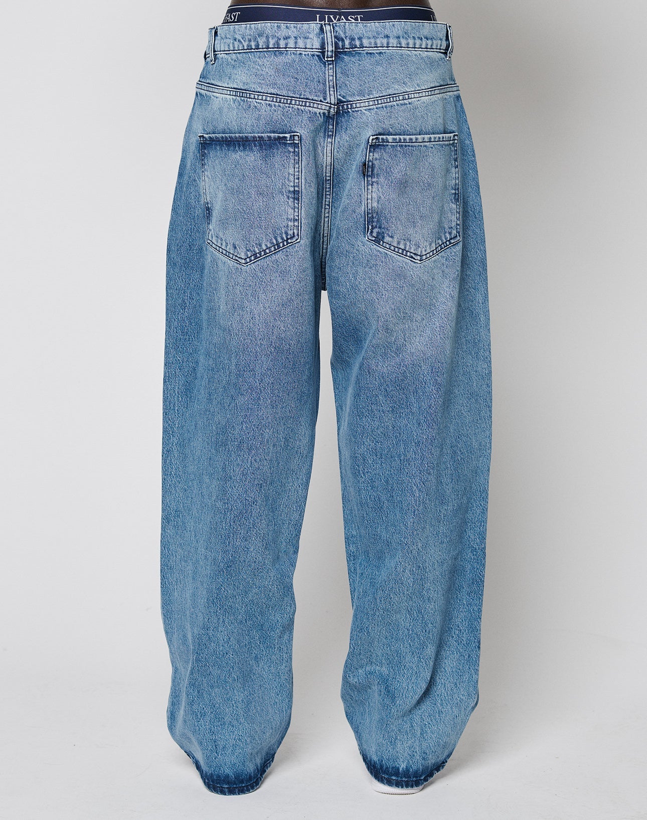 A person seen from the back wears LIVE FAST DIE YOUNG’s LFDY Baggy Denim jeans in light blue with large back pockets, a visible waistband, and a wide straight leg for a relaxed silhouette.