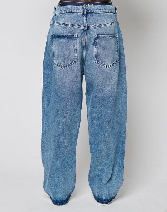 A person seen from the back wears LIVE FAST DIE YOUNG’s LFDY Baggy Denim jeans in light blue with large back pockets, a visible waistband, and a wide straight leg for a relaxed silhouette.