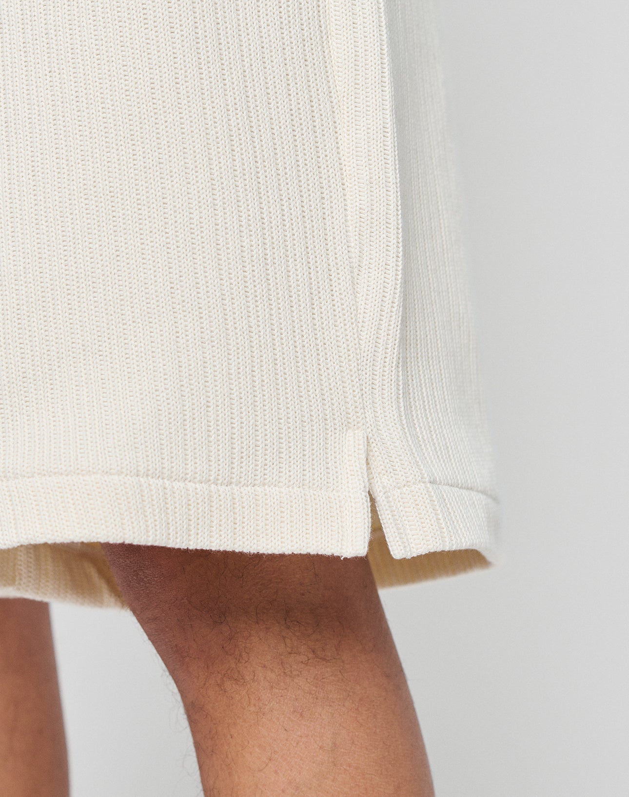 Close-up of the lower part of LIVE FAST DIE YOUNGs Basic Knit Shorts in cream, featuring a ribbed texture, elastic waistband, and small side slit. Shown on medium-brown skin against a plain light background.