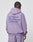 A person with braided hair wears an oversize fit, loose lavender Basic 360 Hooded and matching pants by LIVE FAST DIE YOUNG. Bold LiveFast HvySweat 360g/m² text, plus smaller details, appear on the back. Made from premium cotton-polyester.