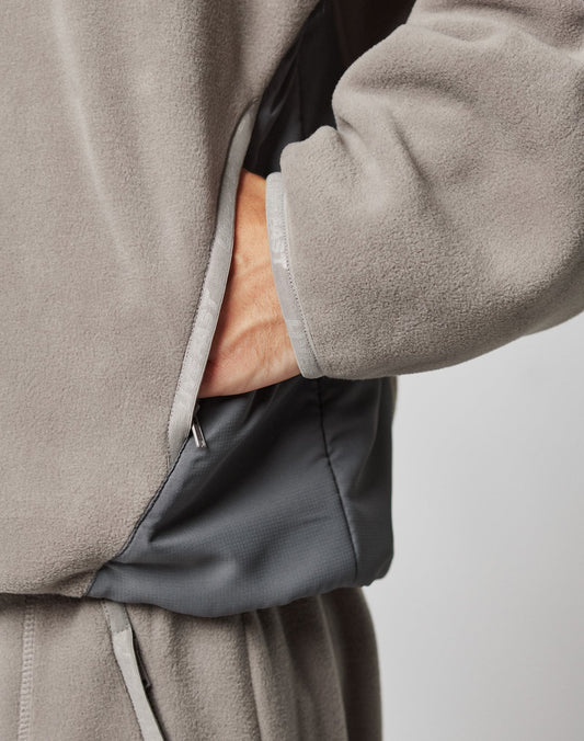 A person wears the LIVE FAST DIE YOUNG Live Fast Fleece Halfzip in soft light gray with nylon details and matching pants, hand in pocket, highlighting the relaxed oversized fit and cozy texture of the outfit.