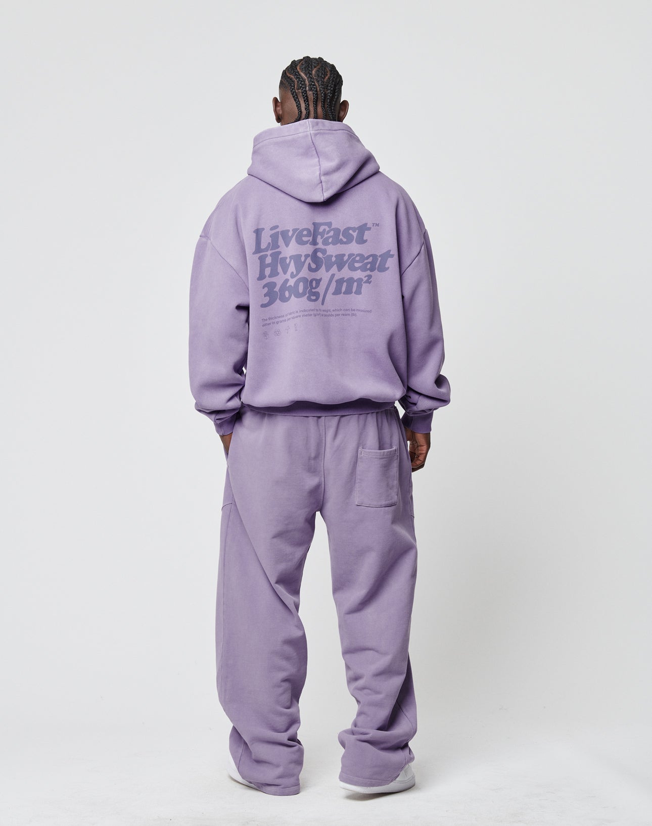 A person faces away in a lavender LIVE FAST DIE YOUNG Basic 360 Hooded and matching sweatpants, both in vintage wash. Bold Live Fast HW Sweat 360g/m² text appears on the hoodie’s back. The background is plain white.