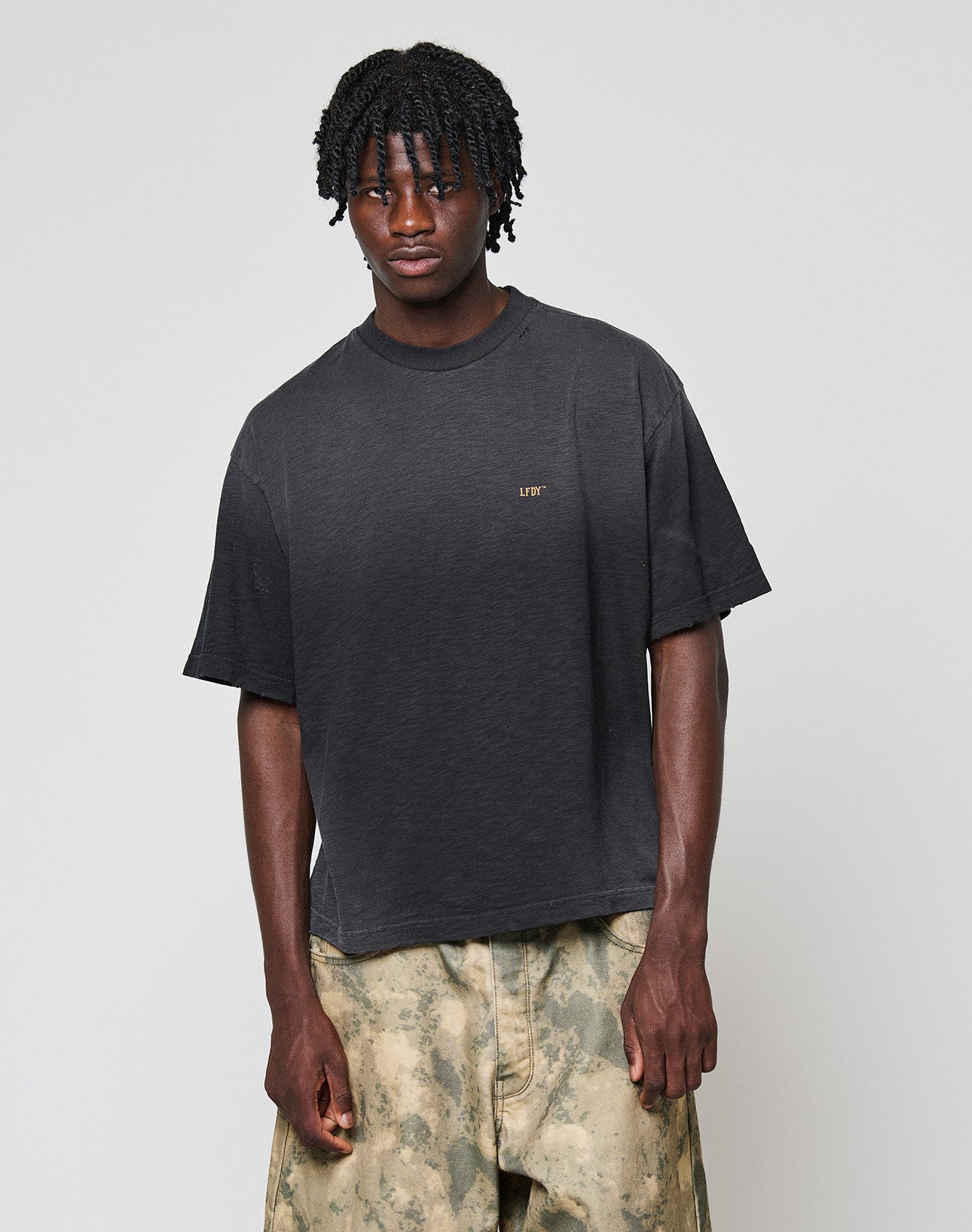 A man with short, twisted hair wears the LIVE FAST DIE YOUNG LFDY Hinterhof Tee in Oversize Fit with small chest text and light green tie-dye pants in Vintage Waschung, standing against a plain white background.