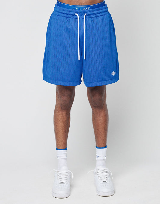 Someone wearing LIVE FAST DIE YOUNG Basic Mesh Shorts in bright blue, paired with white crew socks and white sneakers, stands against a plain light background. Only the lower body is shown.