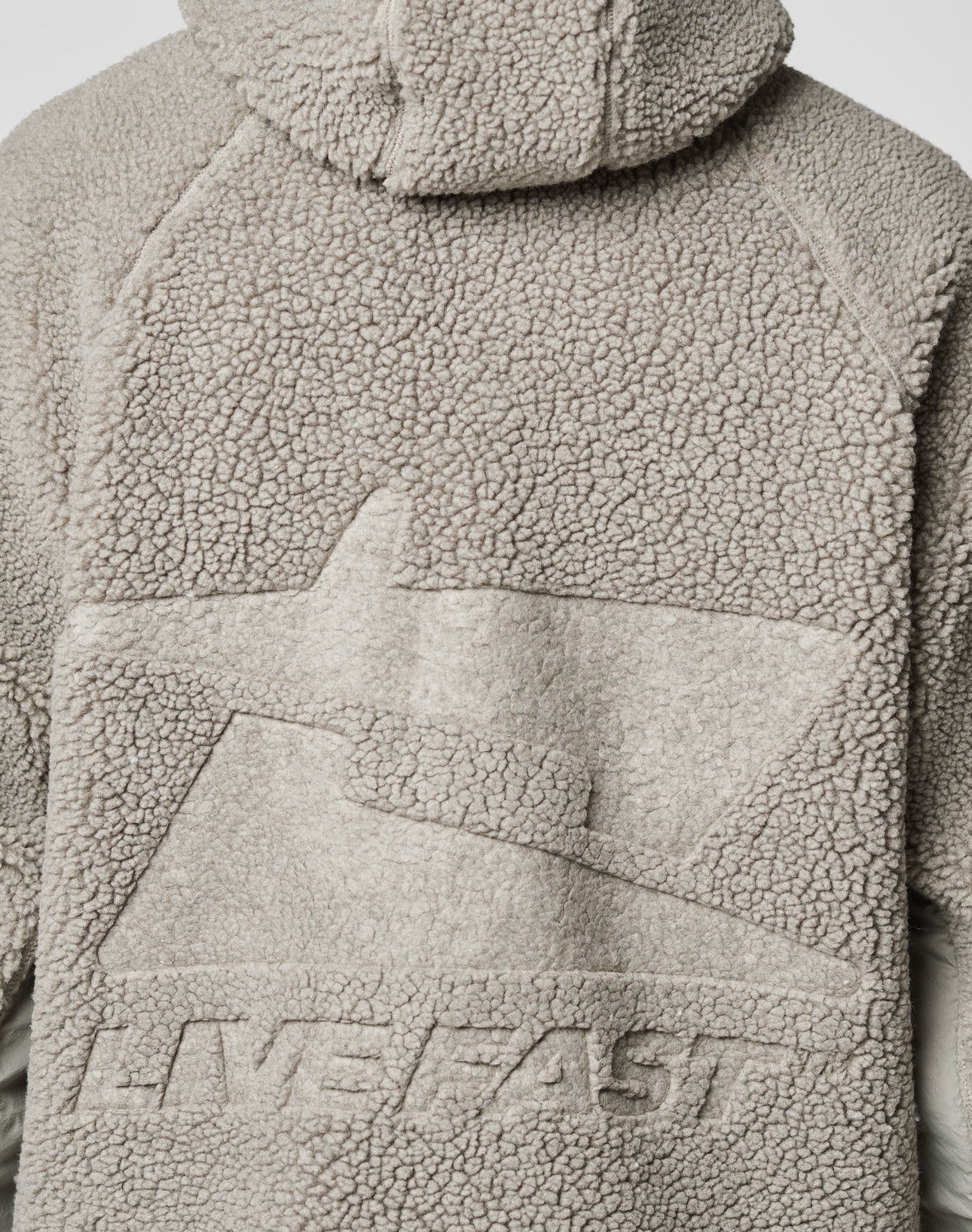 Close-up of the back of the light gray Live Fast Teddy Jacket by LIVE FAST DIE YOUNG, featuring embossed abstract branding and raised “LIVE FAST” text on textured fleece fabric.